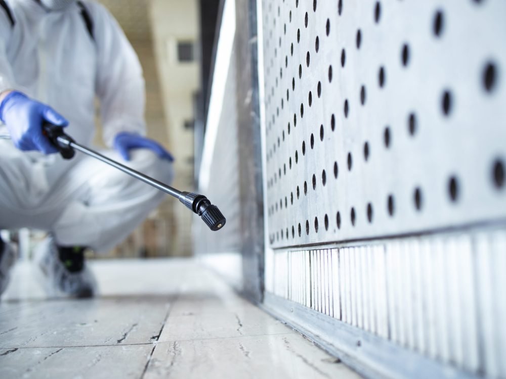 Unrecognizable person in white chemical protection suit doing disinfection of public areas to stop spreading highly contagious corona virus.